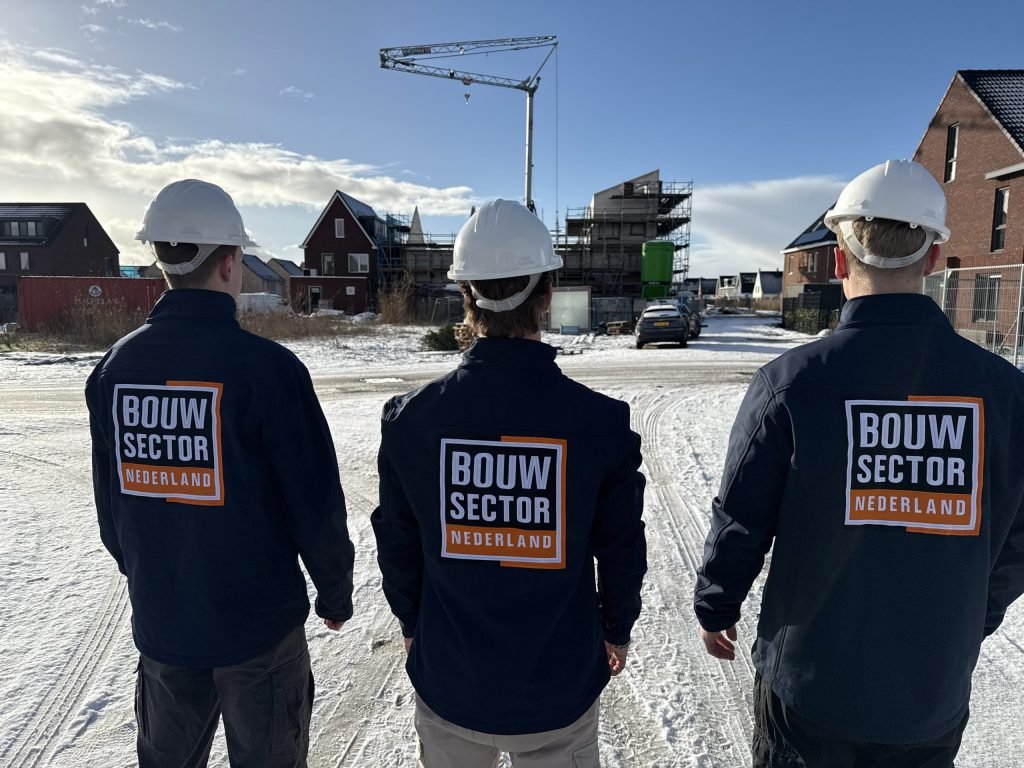 Drie vakmensen van Bouwsector Nederland in werkjas met logo op de rug, op weg naar een klus in een nieuwe woonwijk